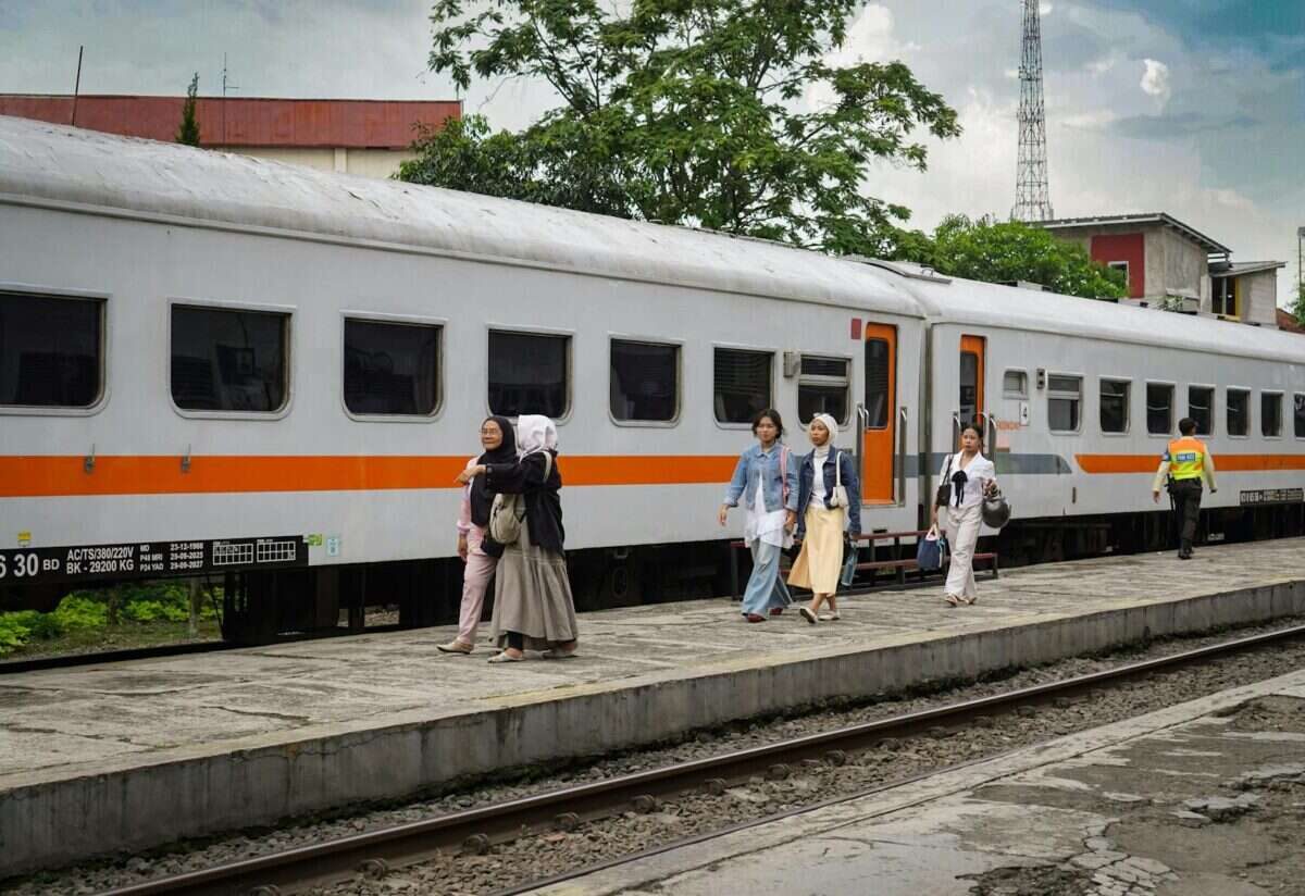 Group of adults walking beside a train at a platform in Bandung, Indonesia, outdoors during the day.