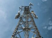 A low-angle shot of a tall metal communications tower with multiple antennas against a clear blue sky.