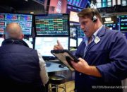 Suasana lantai perdagangan bursa saham Wall Street di New York dengan latar belakang layar indeks pasar yang bergerak variatif.