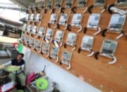Logo PLN Mobile di layar ponsel pintar dengan latar belakang kantor layanan PLN
