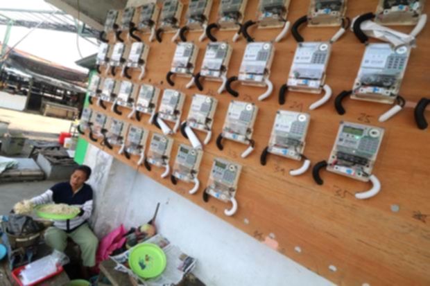 Logo PLN Mobile di layar ponsel pintar dengan latar belakang kantor layanan PLN